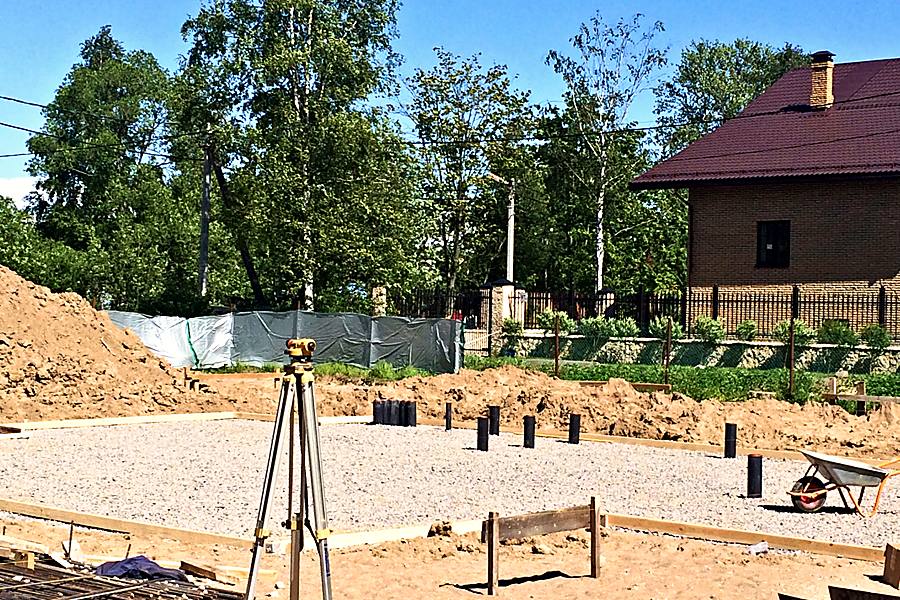 Основание под плиту: щебёночная подсыпка, закладные трубы и нивелир на штативе